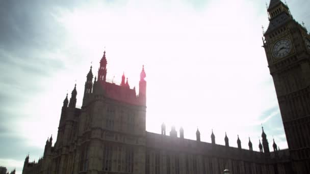 カメラはロンドンのビッグベン時計塔に焦点を当てて 左から右にわずかにパンします 午後に撮影され 太陽はまぶしく 興味深い光の効果を作成します — ストック動画