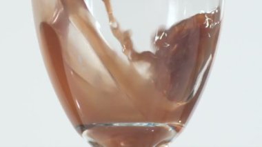 Uzun bir Lale Yavaş close-up Şarap kadehi parlak beyaz ışık ile backdropped ise kahverengi sıvı ile doldurma şeklinde.
