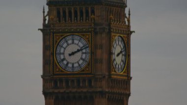 Londra'daki Big Ben saat kulesinin sabit bir yakın çekim, kulenin saat kısmına odaklanıyor. Gri gökyüzü ile çevrilidir..
