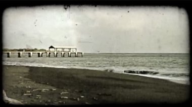 Kıyı kapalı pier Okyanusu ve bulutlar karşı arka planda gökkuşağı Balık tutma insanlarla kırma dalgaların yavaş zoom. Vintage stilize video klip.