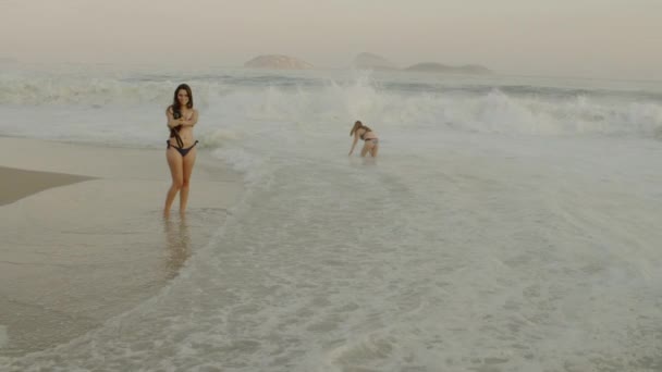 リオデジャネイロ 6月16 2013 ブラジルのリオデジャネイロのイパネマビーチでサーフィンに立っている間 自分の写真を撮るために回る若い女性のスローモーション静的なショット 別の若い女性は 最初の後ろの波で再生します — ストック動画