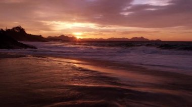 Yavaş çekim, praia do Diabo (Devil's Beach) gün batımında ufukta dağlar ile sörf çöken dalgaların çekim izleme