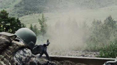 Kemerle beslenen bir makineli tüfeği vururken bir askerin omzunun üzerinden yakın görüş. Kask takıyor. Silah ateşlenirken duman üfler. Yeşil Bereli Abd Ordusu Özel Kuvvetler için bir eğitim gönderen.