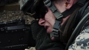 Bir askerin suratından eline doğru hareket eden yakın çekim, kemerle beslenen bir makineli tüfeği vururken tetiği çekerek. Kulak tıkacı, gözlük ve kask takıyor. Yeşil Bereli Abd Ordusu Özel Kuvvetler için bir eğitim gönderen.