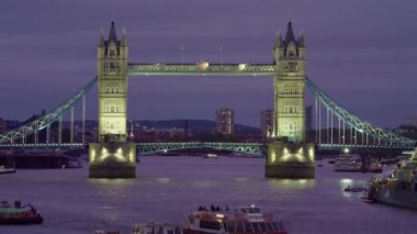 Londra'da Thames Nehri üzerinde Tower Bridge'in sabit bir fotoğrafı. Akşam yakalanan, oldukça karanlık dışında ve köprü kendisi yanar. Thames'te tekneler, köprüde trafik ve arka planda bazı binalar var..