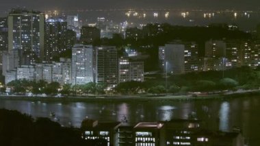 Rio de Janeiro, Brezilya küçük bir yarımadanın kıyısında birçok bina ve bir yol gösteren gece hava zamanı hızlandırılmış. Tekneler suda ve arka planda bir köprü görülebilir.
