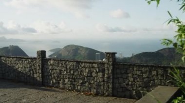 Rio de Janeiro'nun bir gözcü noktasından bir kaydırma, hareketli bir çekim. Kamera tava ve sola hareket eder, sonunda şehrin ve körfez alanının çoğunu ortaya çıkarmak için duvarın üzerinde yükselen.