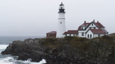 Portland Head ışık ve çevredeki binalara Cape Elizabeth, Maine, kayalık sahil şeridi üzerinde. Yağmur yağıyor ve kulenin tepesinde dönen ışık görülebilir.