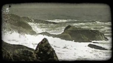 Dalgalar Pasifik Okyanusu'nun yanındaki bir adanın ucundaki büyük yosunlu kayalara çarpar. Vintage stilize video klip.