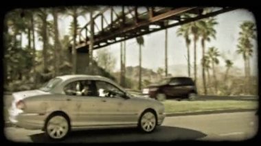 Gümüş, pahalı dört kapı araba hızlı bir şekilde Las Vegas, Nevada dışında bir kırmızı köprü geçit altında ve palmiye ağaçları ile kaplı yolu boyunca kullanıyor. Vintage stilize video klip.