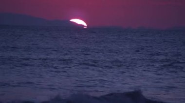 Kosta Rika kıyı şeridi boyunca seyahat eden bir teknenin fotoğrafı. Güneş ufukta yavaşça batarken görülüyor..