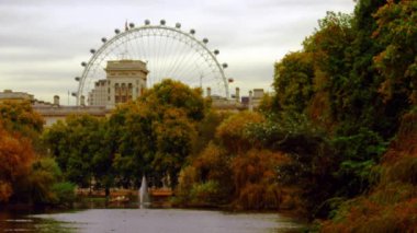 London Eye'ın ve uzaktaki bazı evlerin sabit bir görünümü. Saint James Park'tan çekilen çekimde, içinde çeşme ve kıyılarda ağaçlar bulunan güzel bir sahil de yer alıyor..