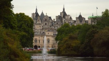 Londra'daki At Muhafızları binasının sabit bir fotoğrafı Saint James Park'tan çekildi. Bazı arabalar sokağa park edilmiş. Parkta çeşmeli ağaçlar ve sahil görülebilir. Bazı kuşlar suda yüzüyor..