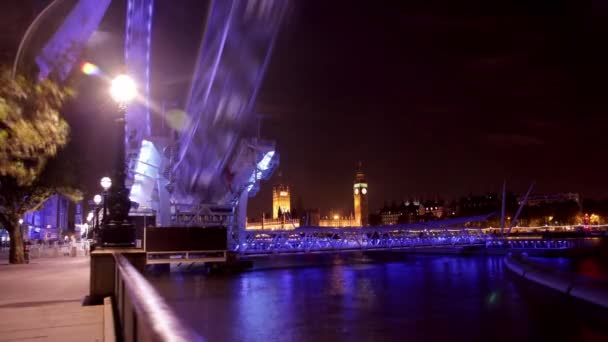 動きはビッグベンと議会の下院を背景にロンドンの目の時間経過をぼかした 観覧車が紫と青の光で照らされる夜に撮影 — ストック動画