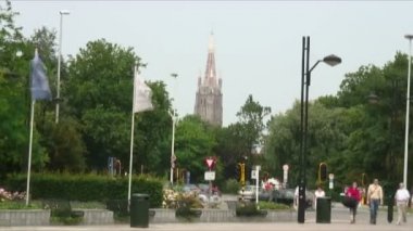 Hızlandırılmış Spire Our Lady kilise ağaçların üzerinden görünen ve bayraklar sallayarak Bruges Belçika'gösterilen.