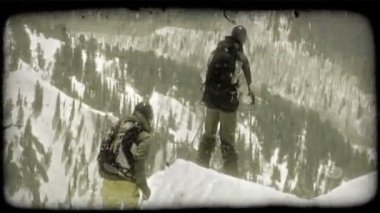 Kayakçılar, bir erkek ve bir kadın, her ikisi de profesyonel dişli giymiş, onlar sadece yokuş aşağı yamaçlara doğru bir dağ zirvesi boyunca slayt olarak yüksek dağ aşağı yolculuğa başlar, uzak dağlar yaprak dökmeyen ağaçlarla kaplı