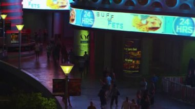 Geceleri açık havada Las Vegas alışveriş merkezinin etrafında dolaşan insanların üstündeki yüksek açılı görüntüler. Kaydırma çerçeveleri ve parlak reklamlar sahneyi aydınlatır. Las Vegas, Nevada'da çekildi.