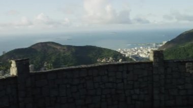 Rio de Janeiro'nun bir gözcü noktasından bir kaydırma, hareketli bir çekim. Kamera tava ve sola hareket eder, sonunda şehrin ve körfez alanının çoğunu ortaya çıkarmak için duvarın üzerinde yükselen.