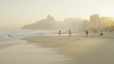 Gün batımında Ipanema plajı boyunca oturan ve yürüyen insanların yavaş çekim izleme çekim. Rio de Janeiro, Brezilya'da çekildi.