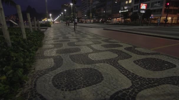 リオデジャネイロ 2013年6月 コパカバーナ歩道パターンのナイトショット ランナーとバイカーは 自転車 ランレーンを使用しています トラフィックは中央値で区切されます 夜に撮影 — ストック動画