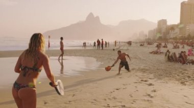 Rio De Janeiro, Brezilya - 24 Haziran 2013: yavaş hareket izleme zemin Vidigal ve altın güneş ışığı altında sahil condos karşı Ipanema Plajı üzerinde Tenis oynayan bir kaç kadeh