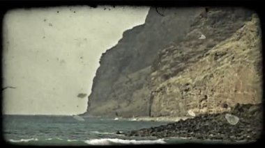 Derin mavi ve yeşil sular ve lav kaya ve kayalık kayalıklar ile kıyıya doğru gelen suyan yana ve arka planda yükselen. Vintage stilize video klip.