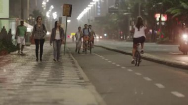 Rio de Janeiro - Haziran, 2013: iki kız kamera doğru yürümek statik çekim, onlar kaldırımda yürüyüş. İşte bir iki şeritli noktalı çizgi ile Bisiklet lane. Kameraya doğru bir turuncu sepet bisiklet ile erkek motorcu.