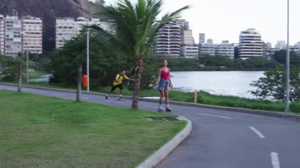 ジャネイロ 2013 スローモーション カップルのローラーブレードと過去の人々 と高層ビルや建物の距離をリオ ジャネイロ ブラジルの通り湖畔ダウン旅行自転車起こっているスケート ボードの追跡ショット — ストック動画