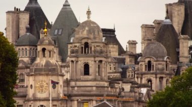 Londra'daki At Muhafızları binasının yakınında kulelerin ve kulelerin sabit bir görüntüsü. Saint James Park'tan çekilen filmde, bazı ağaçlar, bayraklar sallayarak ve gri gökyüzü de görülebilir..