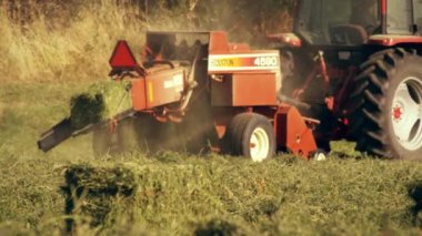 Tarlada dolaşırken saman balyası işleten bir çiftçinin fotoğrafı. Saman balya makinesinin hareketlerini takip ederken kamera soldan sağa doğru hareket eder..