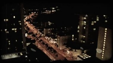 Kırmızı ışık, insanlar ve geceleri palmiye ağaçları ve yüksek binalar ile kaplı araçların meşgul Honolulu sokağa uzun boylu Hotel'den aşağı bakıyor görünümü dolu. Vintage stilize video klip.