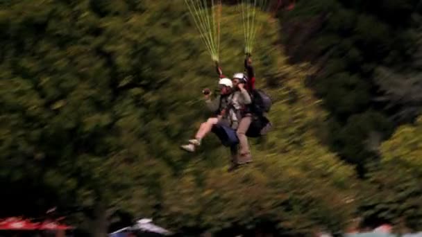 两人串联滑翔伞在瑞士的镜头 相机从右到左移动如下的滑翔伞运动 他们在长满草的地区在城市土地 — 图库视频影像