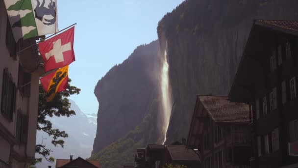 Flaggs Fläktade Vinden Förgrunden Som Vattenfall Brusar Bakgrunden Schweiziska Byggnader — Stockvideo