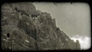 Soğuk dağ tepe kenarı boyunca dağ yarıklar ve cliff çıkıntıları kapalı kayalar ve ağaçlar dağ bulutlu, mavi arka plan ile hızlandırılmış yüzü boyunca üzerinde rüzgar esiyor gibi yağan kar ile soğuk kışın.