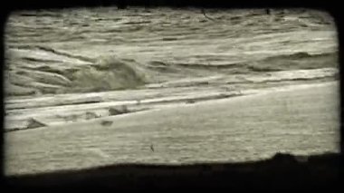 Dalgalar altın ışıkta kumlu plaja karşı kırılır. Vintage stilize video klip.