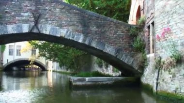 Bruges, Belçika'da bir kanalın üzerinde taş köprünün altından geçiyor. Yukarıda, köprüde insanlar var..