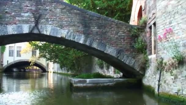 ベルギーのブルージュの運河に架かる石橋の下を行く 橋の上に人がいる — ストック動画