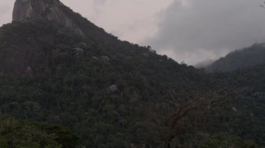 Rio de Janeiro'daki Corcovado'nun tepesindeki İsa heykeline doğru yukarı doğru kaydıran bir atış. Kamera yukarı kaydırıyor ve sola, ağaçlarla kaplı bir tepeye çıkıyor. Bulutlu.