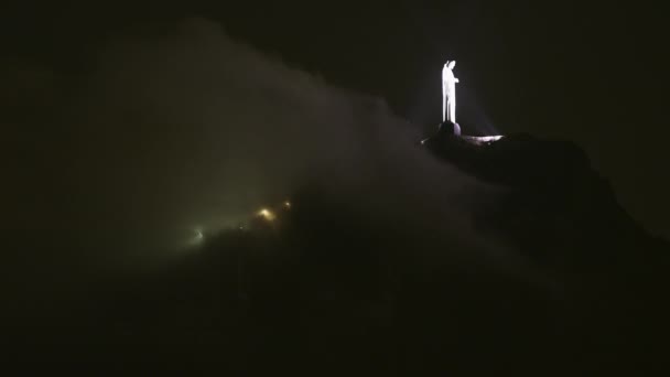 夜コルコバードの遠いキリスト像の静的なショット ライトをともしている彫像と風が吹いて 像の前での周りいくつかの雲 — ストック動画
