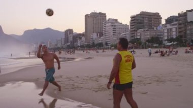 Rio De Janeiro - Haziran 2013: Yavaş hareket pan, Rio De Janeiro Ipanema plajda iki erkek dolly gün batımında futbol oynarken (Abd) veya futbol (Uluslararası) Vidigal silueti karşı