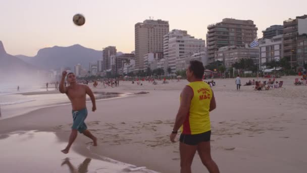 リオデジャネイロ 2013年6月 スローモーションパン リオデジャネイロのイパネマビーチで2人の男性のドリーは 日没時にサッカー アメリカ またはサッカー をヴィディガルのスカイラインに対して再生します — ストック動画