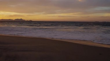 Yavaş çekim, köpüklü dalgalar Praia do Diabo (Devil's Beach) alacakaranlıkta akarken kum boyunca çekim izleme