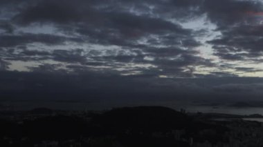Soldan sağa doğru Rio de Janeiro şehrine üzerinde tava bir atış. Güneş ve şehrin karartma. Gökyüzü ve bulutlar şehri iken çerçevenin üst üçte defne makyaj ve kontrast dağlar alt üçüncü doldurun.