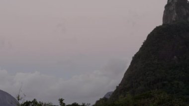 Rio de Janeiro, Brezilya üzerinde Corcovado İsa'nın yukarı kaydırma çekim. Kamera, heykel çerçevenin ortasına gelene kadar tepenin sağ ve yukarısında yer almaktadır. Gökyüzü bulutlarla dolu..