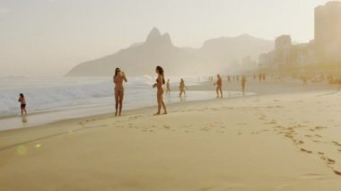 Rio De Janeiro, Brezilya - Haziran 2013: Yavaş çekim, Ipanema plajında bikinili iki genç kadının güneş gözlüğü takarak ve altın güneş ışığında fotoğraf çekmenin 180 izleme fotoğrafı