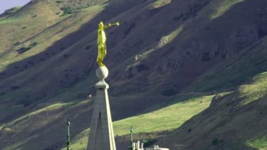 Angel Moroni'nin altın renkli heykeli, Lds Salt Lake Tapınağı'nın üzerine doğuya doğru işaret eder. Yeşil ve kahverengi dağlar arka planda görülebilir.