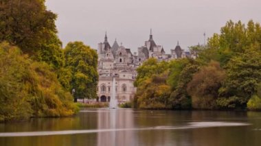 Hızlandırılmış günbatımı Londra'daki St. James's Parkı gölde. Ağaçlı gölde bir çeşme vardır. At arka planda bina gardiyanlar yanar ve gün geceye bakılırsa göle yansıtır.