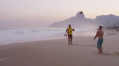 Rio De Janeiro - Haziran 2013: Yavaş hareket pan, Rio De Janeiro Ipanema plajda iki erkek dolly gün batımında futbol oynarken (Abd) veya futbol (Uluslararası) Vidigal silueti karşı