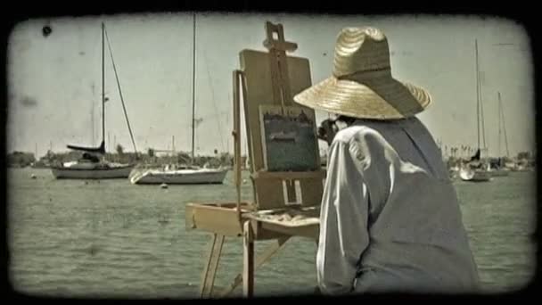 彼女は慎重に海の演出を塗るし 密閉の端から固定された船ドック カリフォルニア州のニューポートビーチの近く青いシャツと太陽帽子に身を包んだ女性のアーティストのワイド ショット — ストック動画