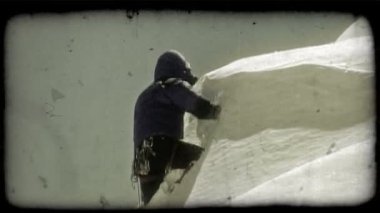 Dağcı, güneşli bir günde derin kar tozuyla kaplı bir tepeye tırmanıp tırmanırken kendini zorlamak için tırmanma direğini kullanır. Vintage stilize video klip.